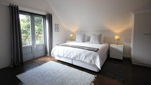 Un dormitorio con una cama grande, dos mesitas de noche, una ventana con cortinas y vistas al verdor exterior.