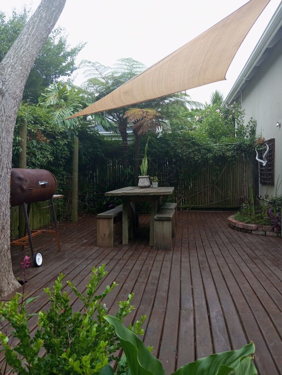 Une terrasse en bois avec une table et des chaises, entourée d’une végétation luxuriante et d’une clôture en bois.
