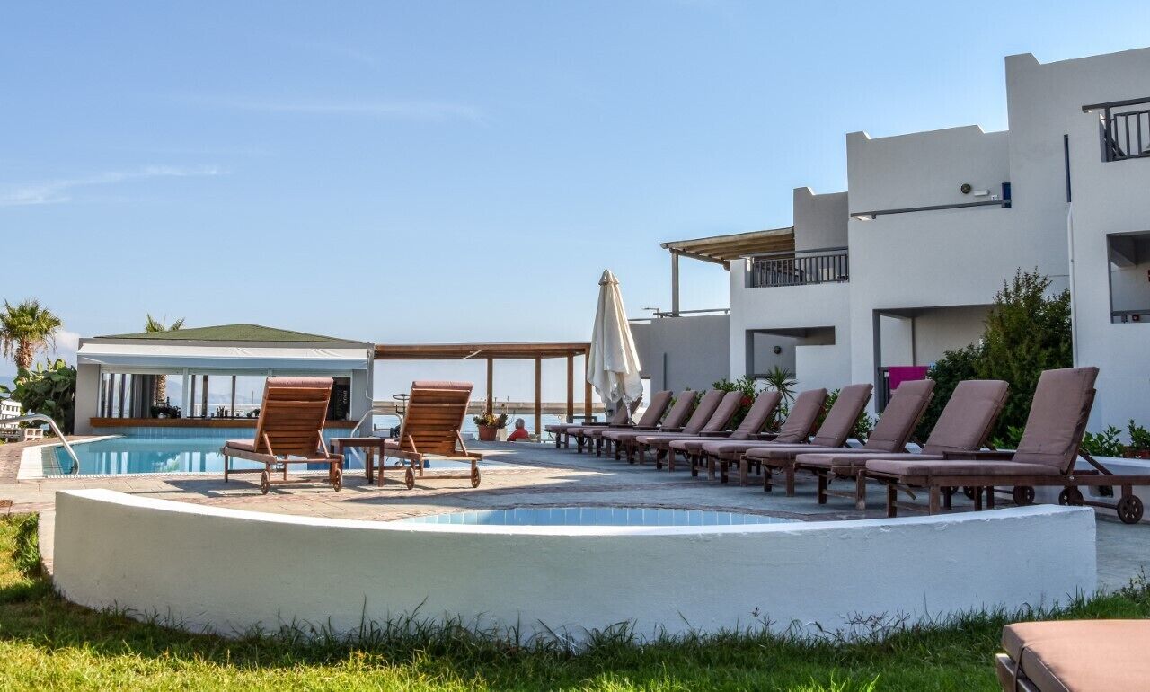 Zona de piscina con sillones de descanso y un edificio con balcones.