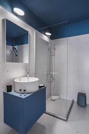 A modern bathroom with a large mirror, a round sink, a shower enclosure, and a blue vanity. - Yria Beach Hotel (Hersonissos)