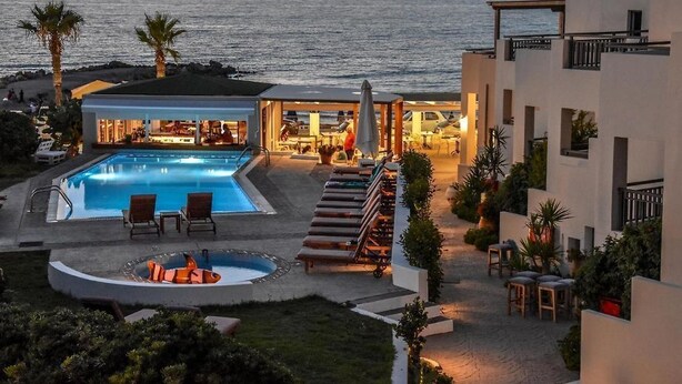 Een resort met een zwembad, ligbedden en uitzicht op zee bij zonsondergang.