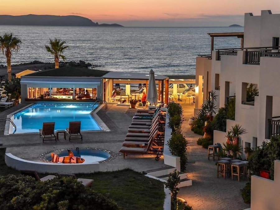 Ein Resort mit Pool, Liegestühlen und Blick auf das Meer bei Sonnenuntergang.