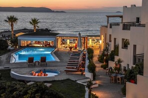 Een resort met een zwembad, ligbedden en uitzicht op zee bij zonsondergang.