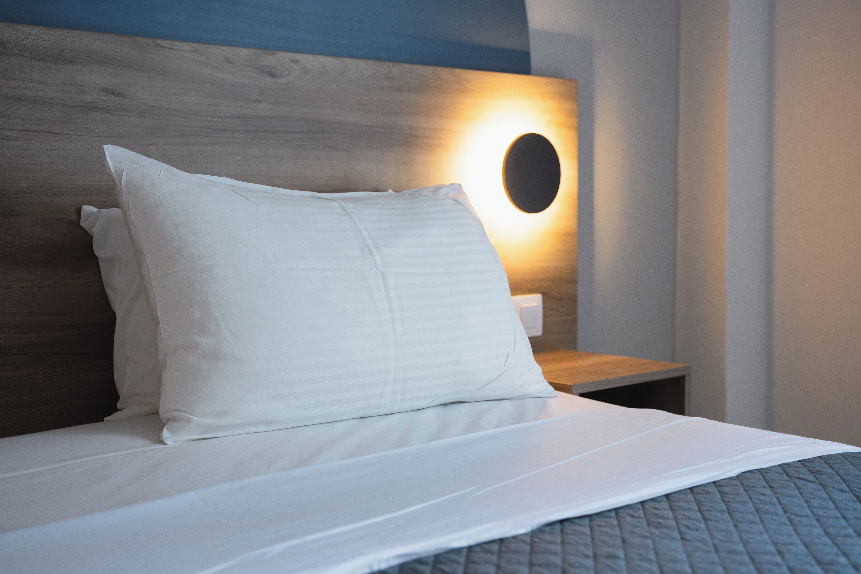 Una cama bien hecha con sábanas blancas y una manta acolchada gris.