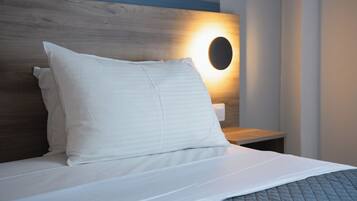 Una cama bien hecha con sábanas blancas y una manta acolchada gris.