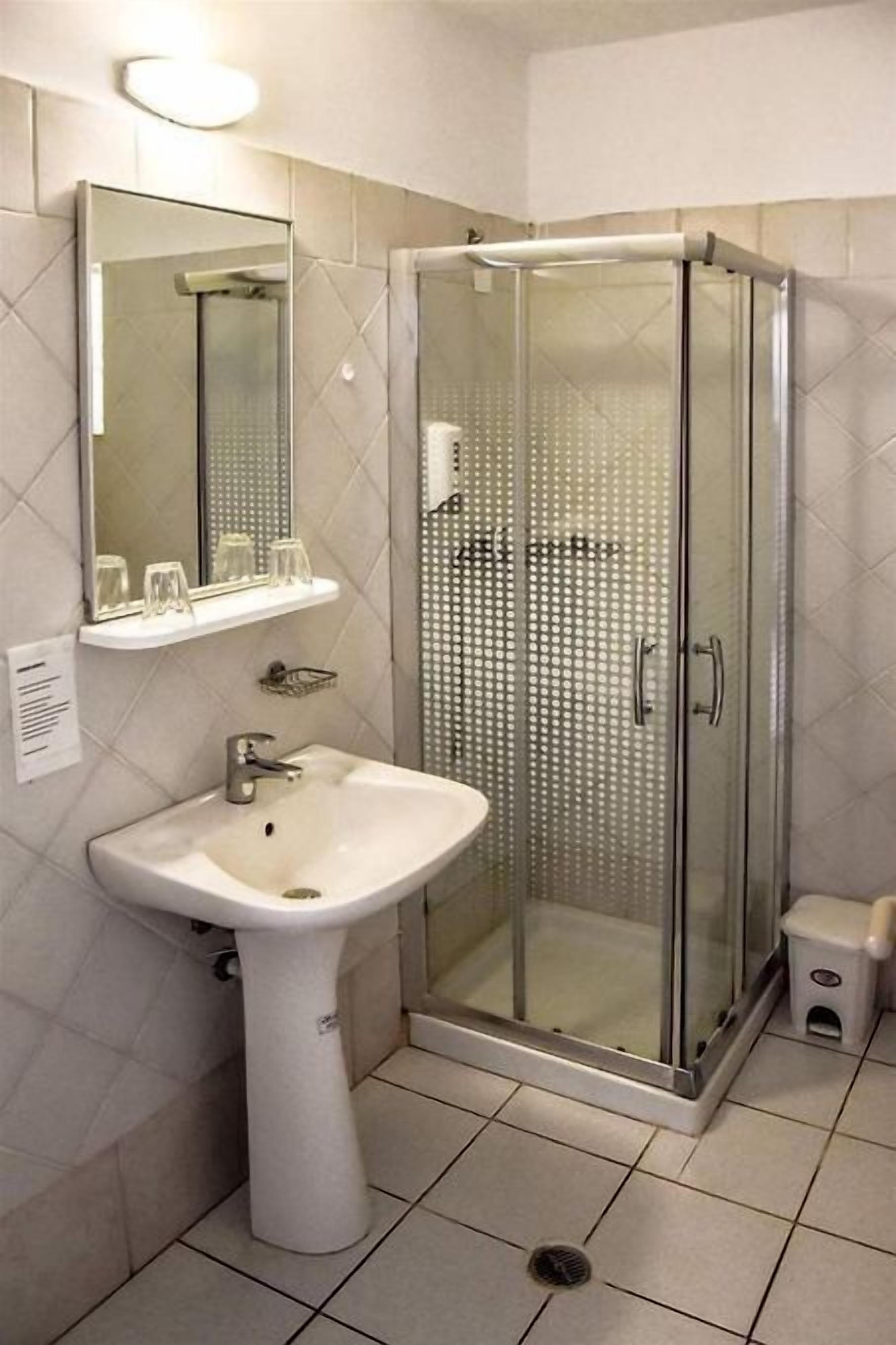 A modern bathroom with a glass-enclosed shower, a pedestal sink, and a mirror above the sink.