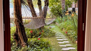 Eine Hängematze zwischen Bäumen in einem Garten mit einem Kiesweg und viel Grün.