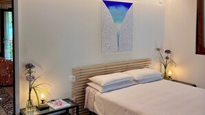 Ein Schlafzimmer mit Holzbalkendecke, einem Bett mit weißer Bettwäsche, einem Nachttisch mit Lampe, einer Vase mit Blumen und einem Wandbild.