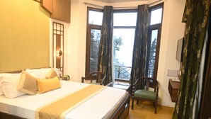 Habitación de hotel con una cama grande, una mesita, una silla y un balcón con cortinas.