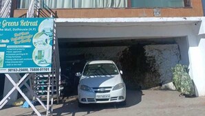Edificio de dos pisos con un letrero que anuncia 'The Greens Retreat', promocionando comodidades como propiedad libre de cargas, estacionamiento común y un lado soleado.
