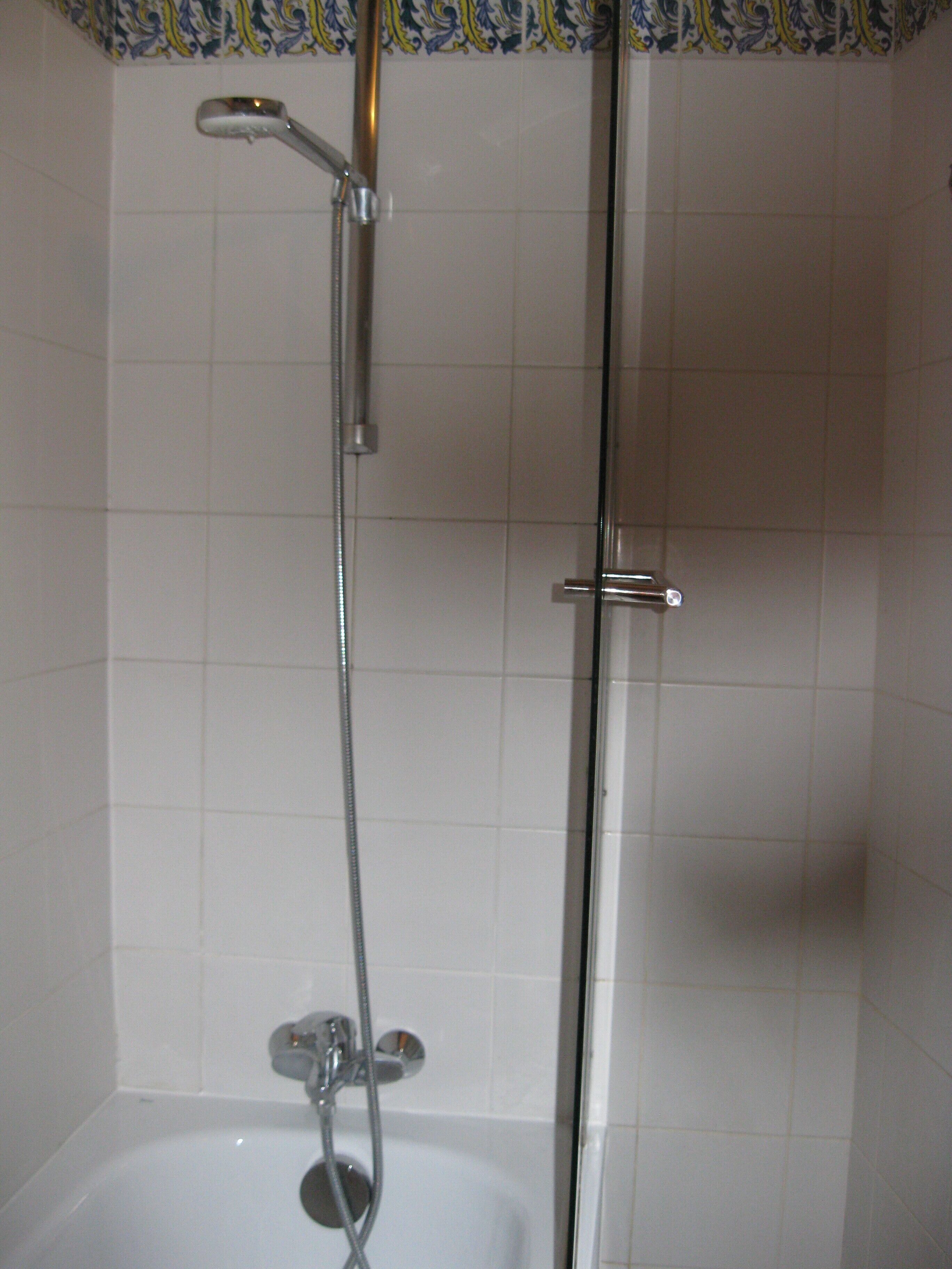 A shower with a handheld showerhead and a wall-mounted faucet.