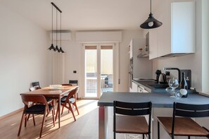 A modern kitchen with a dining area, featuring a large island, pendant lights, and a view to an outdoor balcony. - Home23 Exclusive Holigarda (Desenzano del Garda)