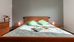 A neatly made bed with a wooden headboard, two green pillows, and a tray with a cup and a pastry on the bed.