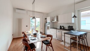 A modern kitchen with white cabinets, a dining area with a wooden table and chairs, and a view of the outdoors through a large window.