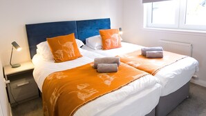 Una cama doble con cabecera azul, dos almohadas naranjas y una manta naranja a juego.