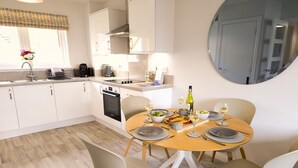 Una cocina moderna con armarios blancos, un comedor con una mesa redonda y sillas, y un espejo grande en la pared.