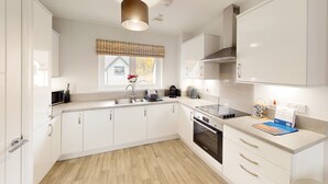Una cocina moderna con armarios blancos, un lavamanos de acero inoxidable, un horno empotrado y una cocina de inducción negra.