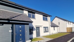 Una hilera de casas modernas de dos pisos con fachada gris y blanca, una puerta azul y un cielo azul despejado al fondo.