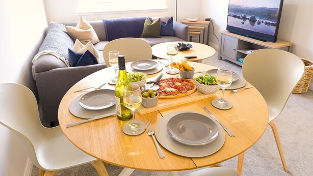 Un comedor con una mesa redonda dispuesta para dos personas, mostrando pizza, ensalada y copas de vino.
