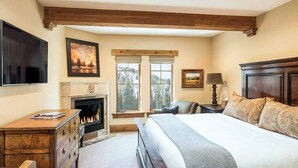 Een slaapkamer met een groot bed, een open haard, een televisie en een bureau.