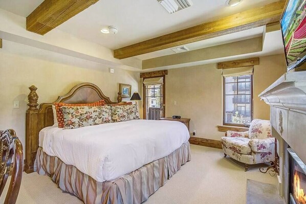 A bedroom with a large bed, a wooden headboard, a fireplace, and a window with a view.