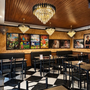 A restaurant interior with wooden ceiling, black and white checkered floor, black and white chairs, and chandeliers. - Hotel Priyadarsini (Bankura)