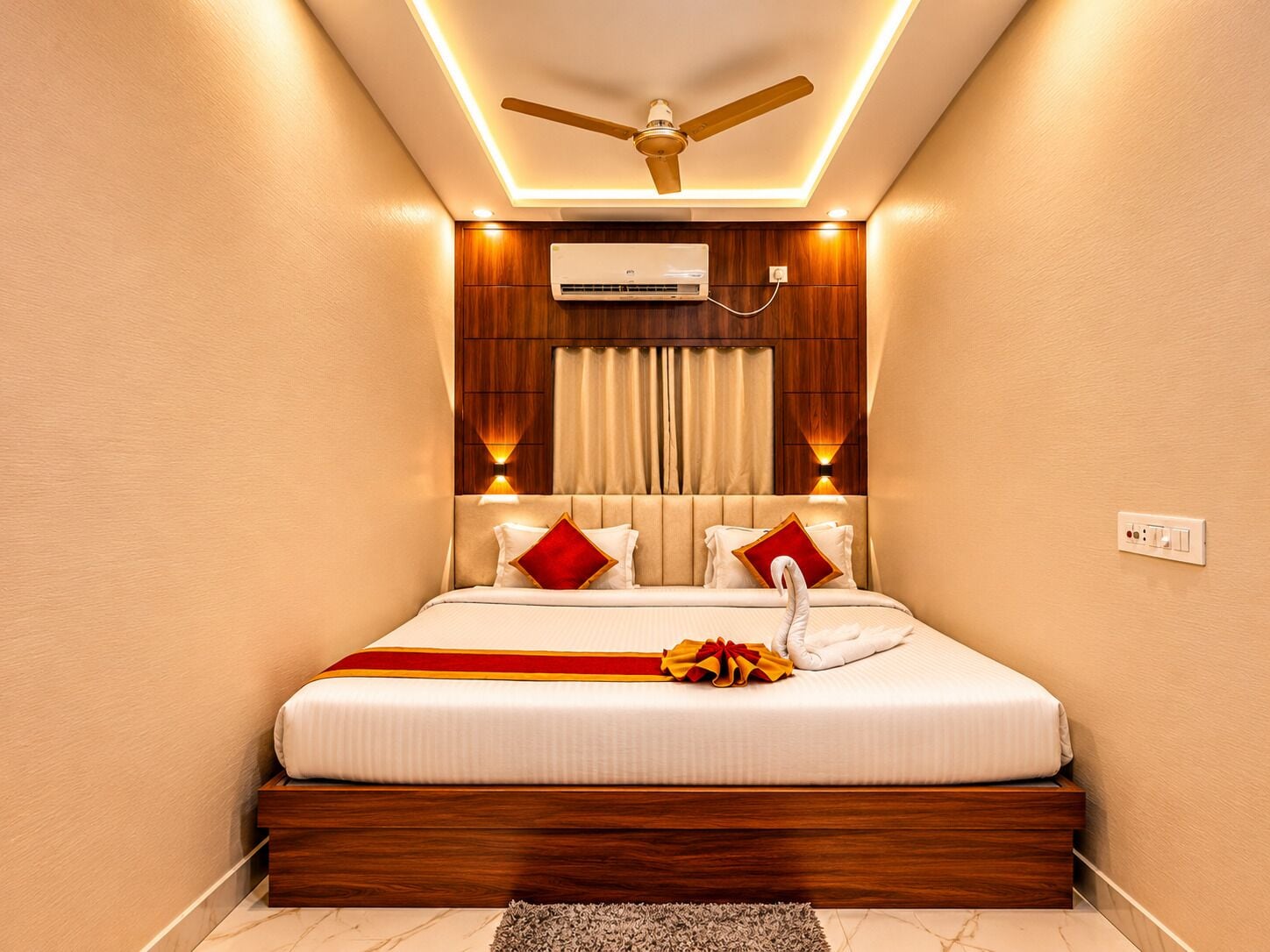 A bedroom with a bed, a ceiling fan, an air conditioning unit, and a power outlet on the wall.