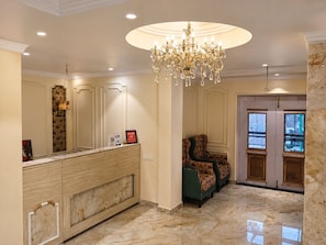 A hotel lobby with a marble floor, a reception desk, a chandelier, and a seating area with patterned upholstery. - Hotel Priyadarsini (Bankura)