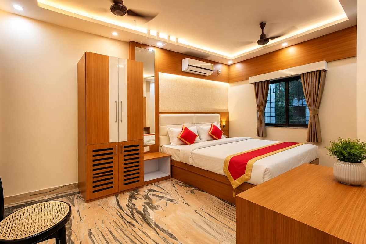 A hotel room with a bed, a desk, a chair, an air conditioning unit, and a window with curtains.