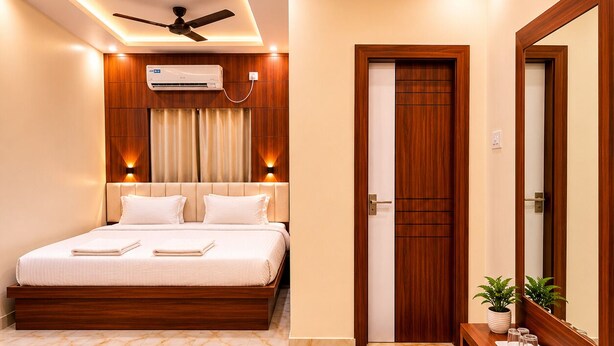 A hotel room with a bed, a ceiling fan, an air conditioning unit, a wooden door, a mirror, and a small plant on a side table. - Hotel Priyadarsini (Bankura)