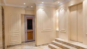 A hallway with marble flooring, a wooden door, and a set of marble steps leading to a room. - Hotel Priyadarsini (Bankura)