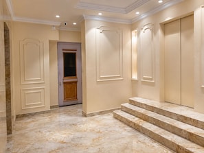 A hallway with marble flooring, a wooden door, and a set of marble steps leading to a room. - Hotel Priyadarsini (Bankura)