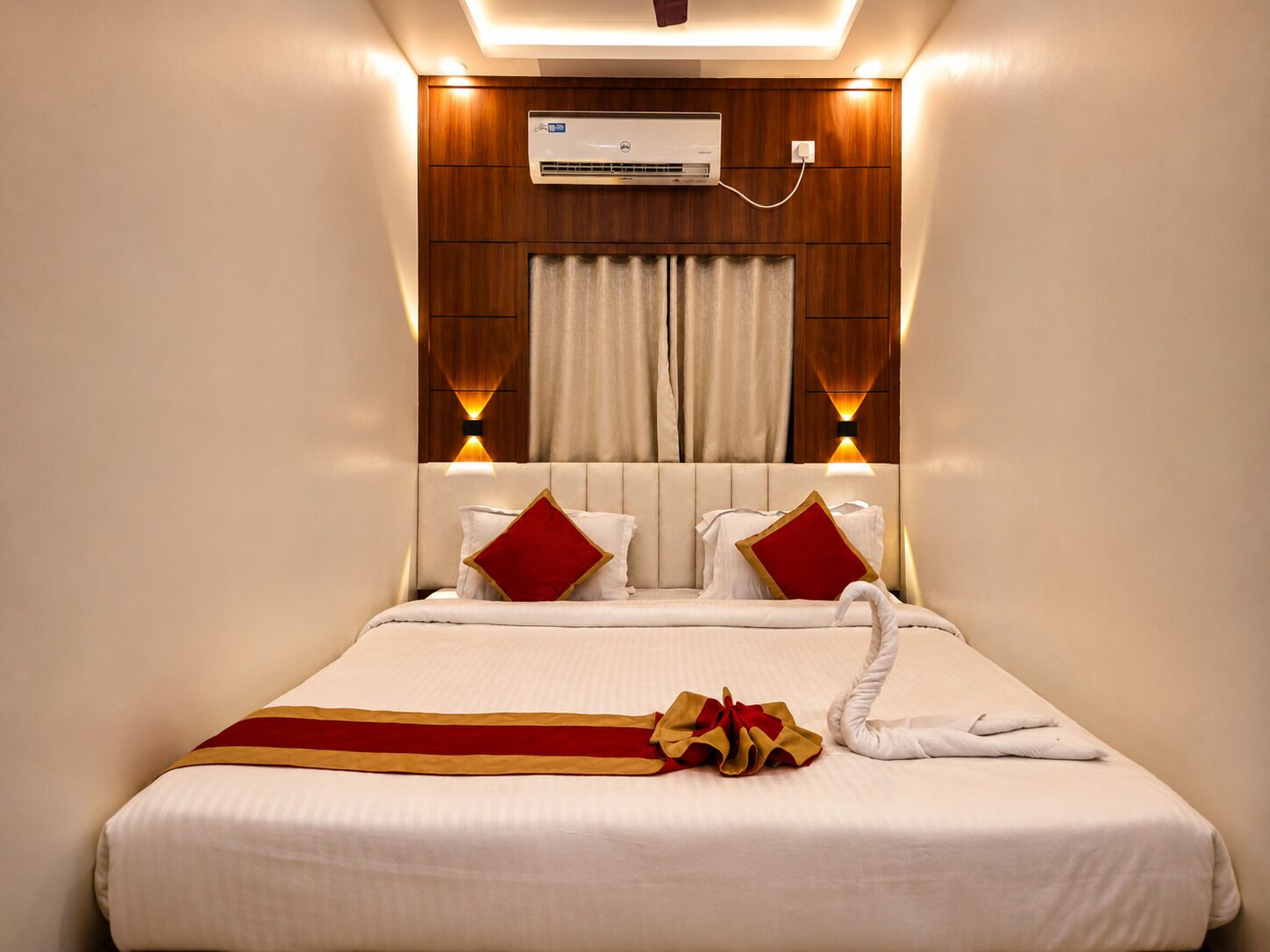 A hotel room with a bed, a wall-mounted air conditioner, and a decorative towel on the bed.