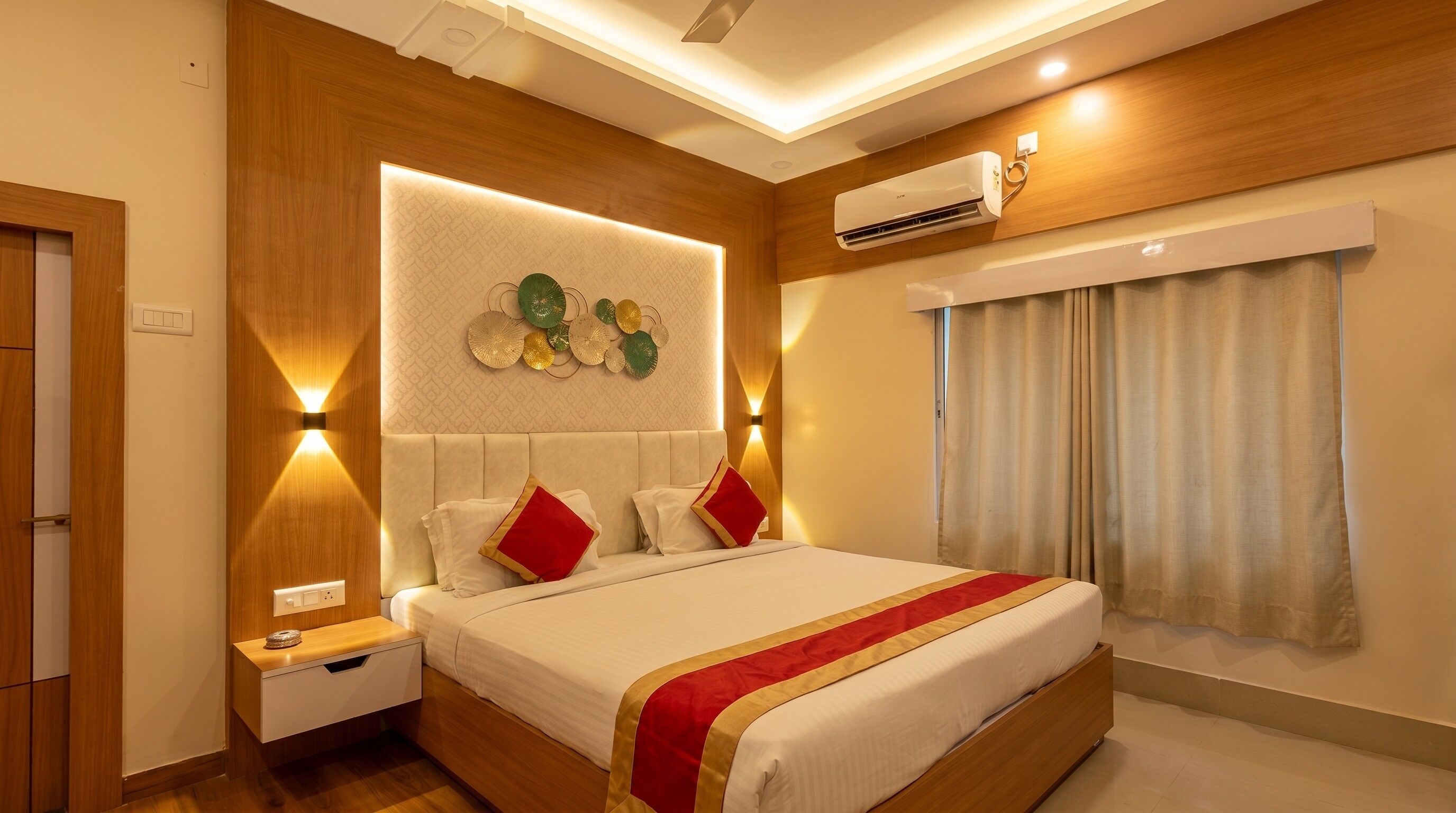 Habitación de hotel con cama, mesita de noche, aire acondicionado instalado en la pared y ventana con cortinas.