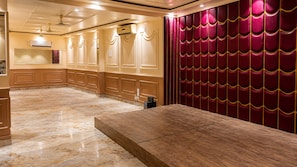 A hotel lobby with a marble floor, a wooden reception desk, and a red upholstered wall with a patterned design.