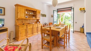 A dining area with a wooden table and chairs, a television on the left, and a cabinet with dishes.