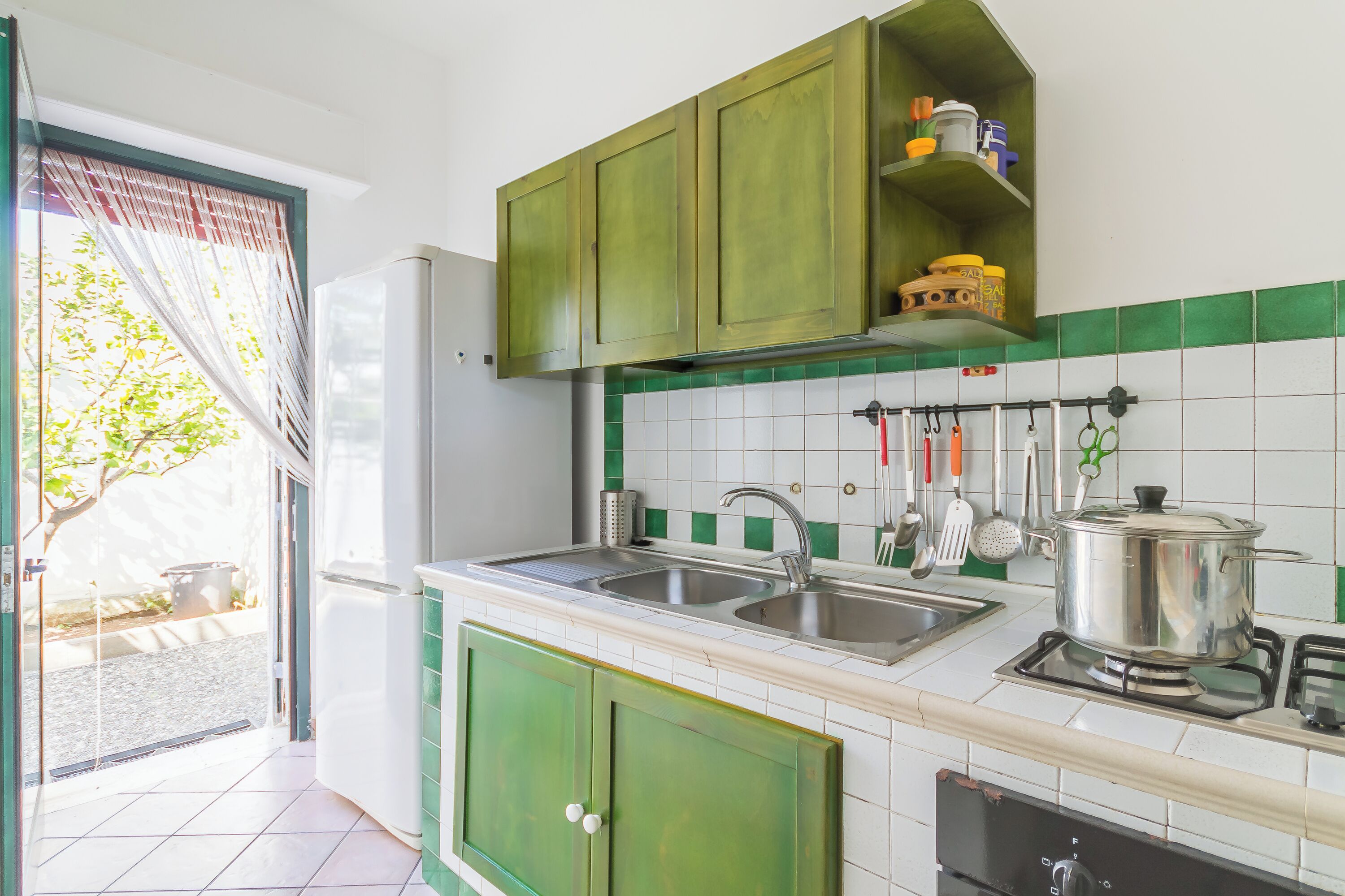 A kitchen with green cabinets, a sink, a stove, and a window with a view of the outdoors.