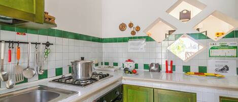 Una cocina con gabinetes verdes, un lavamanos de acero inoxidable y una estufa a gas.