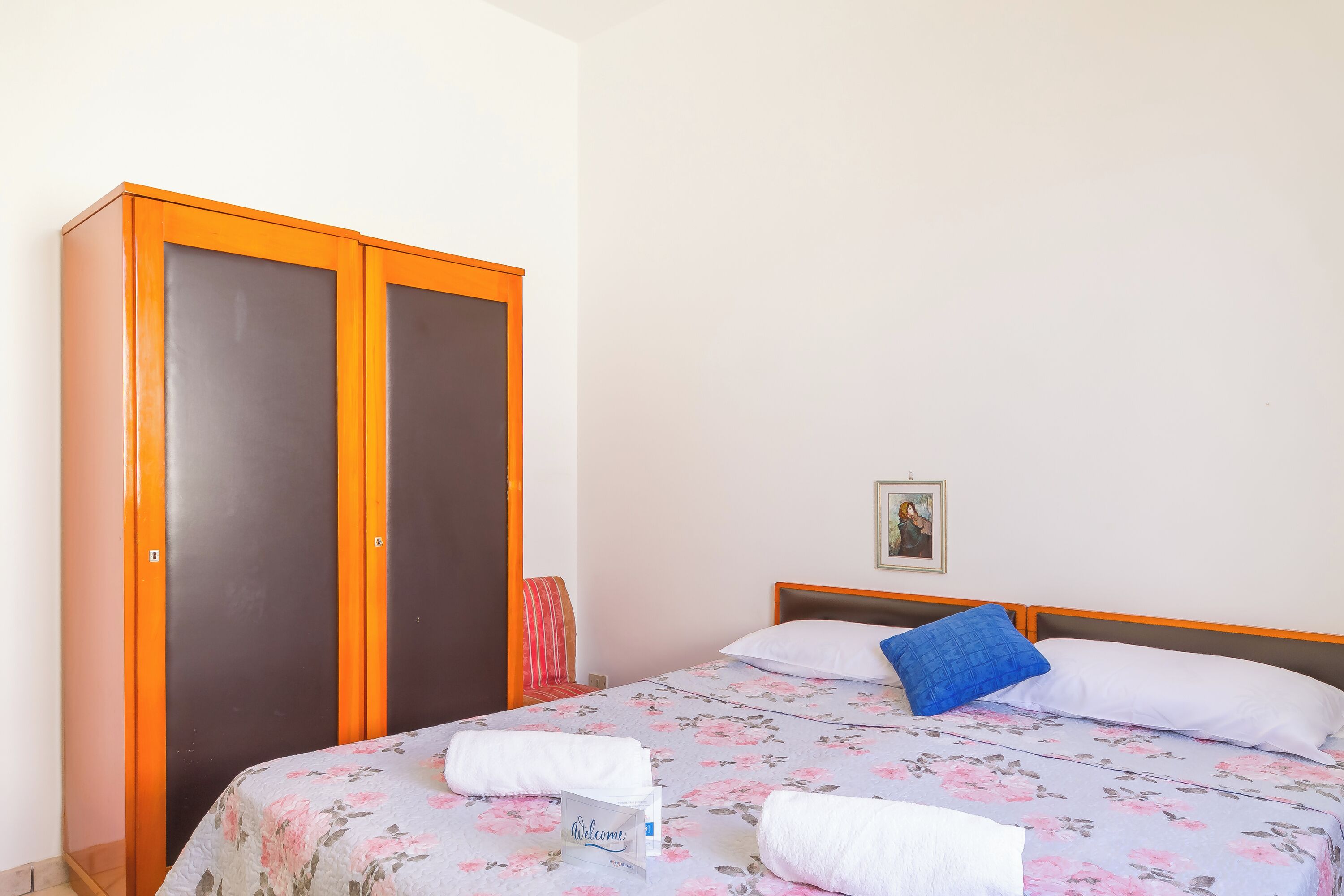 A hotel room with a bed, a wardrobe, and a welcome sign.