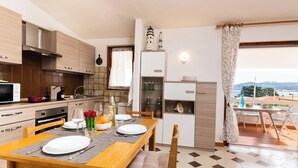 A modern kitchen with wooden cabinets, a dining table set for four, and a view of the sea through a balcony. - La Lampara House (Arzachena)