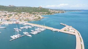 An aerial view of a marina with multiple boats docked, a pier, and a coastal town in the background. - La Lampara House (Arzachena)