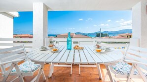 A white table with chairs on a balcony, a bottle, and plates with food. - La Lampara House (Arzachena)