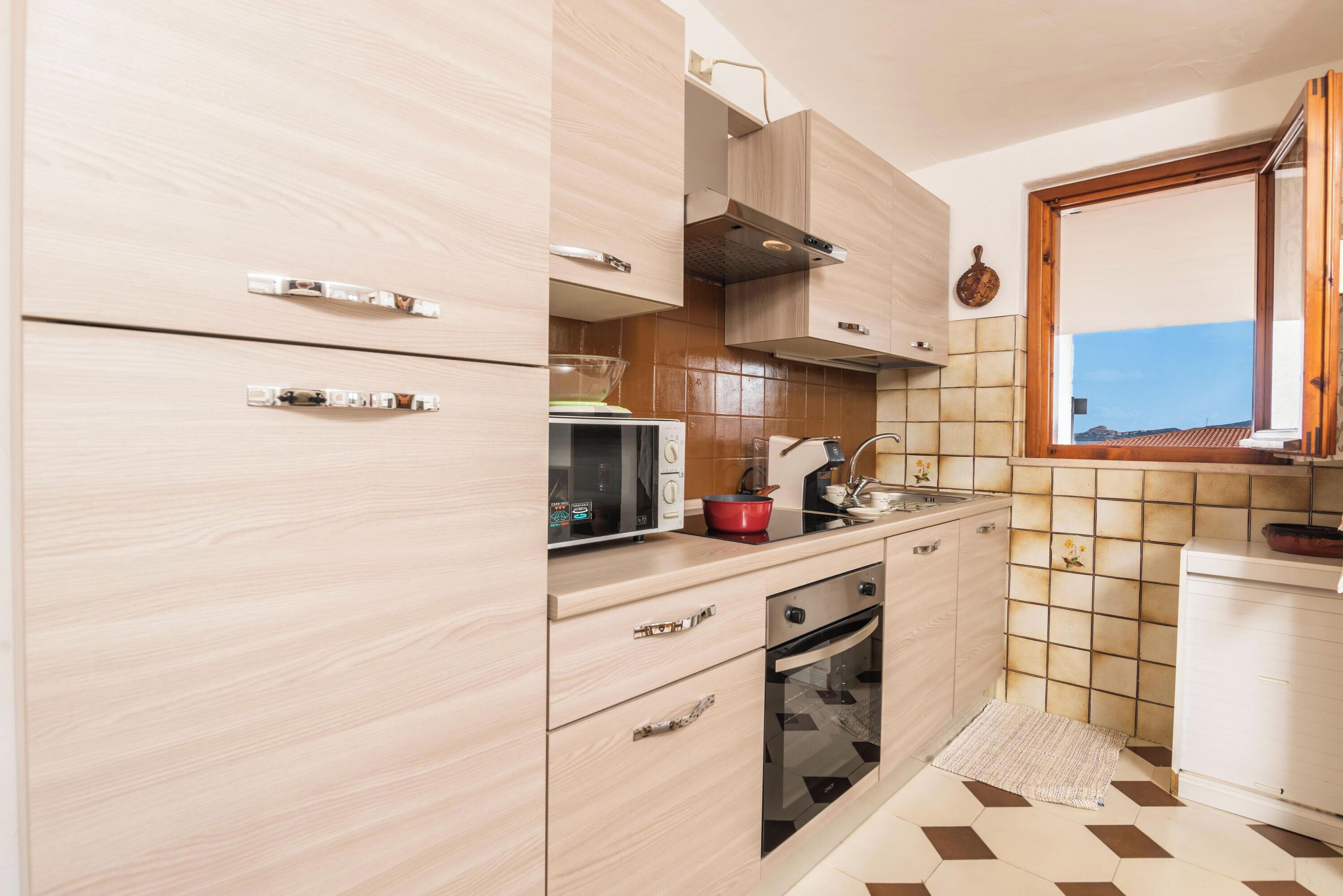 A compact kitchen with light wood cabinets, a microwave, a stove, and a sink.