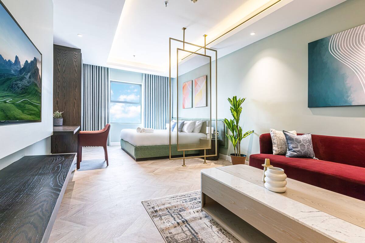 Ein modernes Hotelzimmer mit einem großen Bett, einem roten Sofa, einem Holztisch und einem großen Fenster mit Blick auf die Berge.