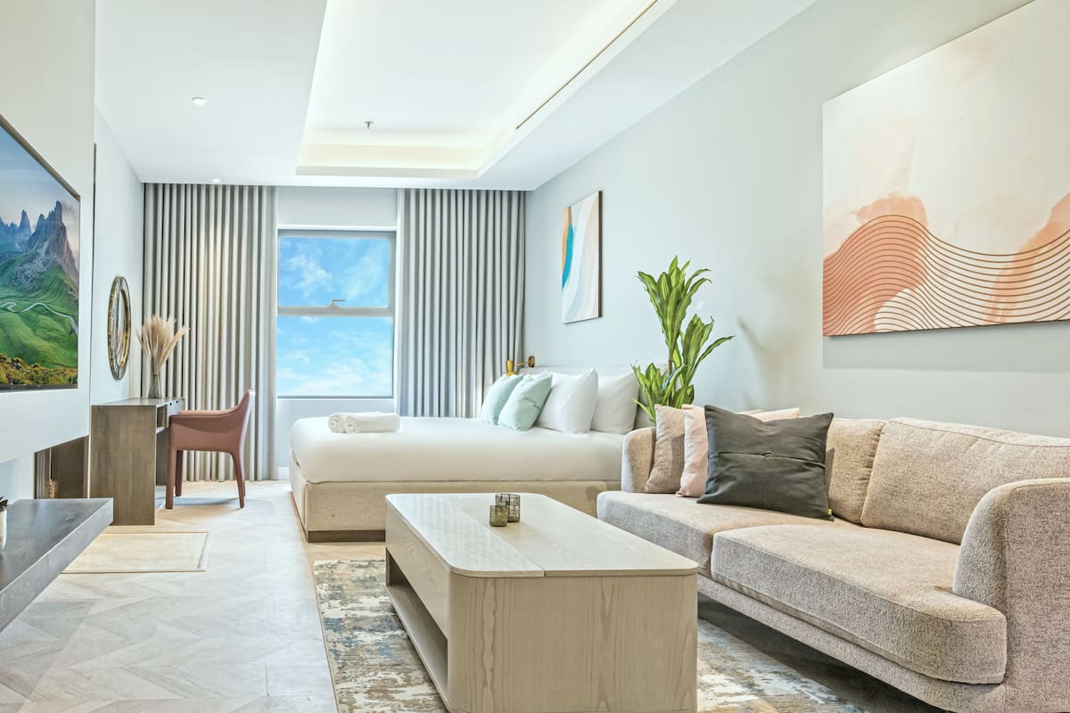 Ein modernes Wohnzimmer mit einer Couch, einem Couchtisch und einem Sessel. Es gibt ein großes Fenster mit Vorhängen, ein Bild an der Wand und eine Pflanze.