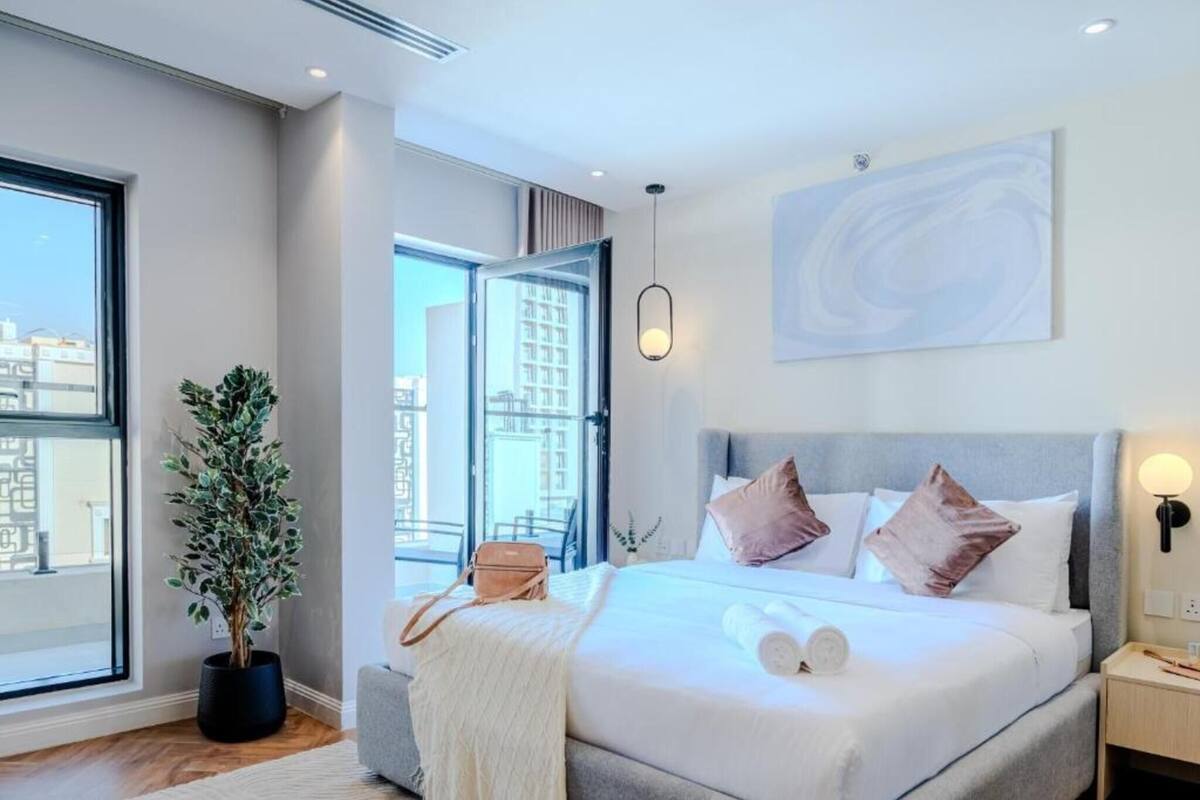 Ein modernes Hotelzimmer mit einem großen Bett, einer Topfpflanze, Blick auf die Stadt und einem großen Fenster.