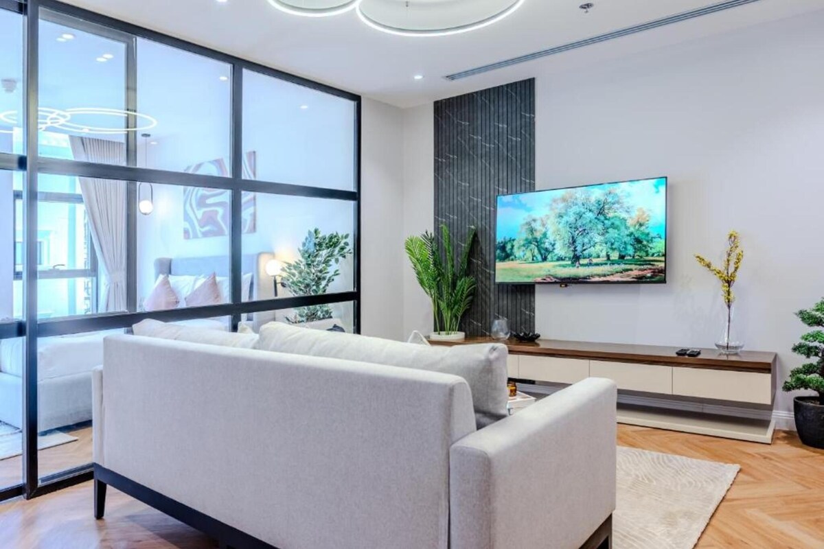 A modern living room with a large window, a flat-screen TV mounted on a wall, and a minimalist sofa.