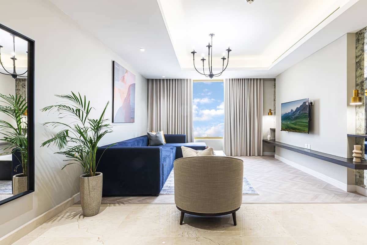 Ein modernes Wohnzimmer mit einem blauen Sofa, einem runden Sessel, einer großen Topfpflanze und Blick zum Himmel durch das Fenster.