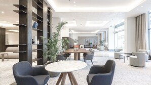 Un hall d’hôtel moderne doté d’un espace de restauration central, de différents types de sièges et d’une grande fenêtre laissant entrer la lumière naturelle.