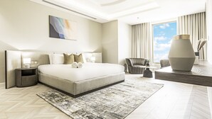 Une chambre d’hôtel moderne avec un grand lit, un coin salon avec un fauteuil, un grand vase et un tableau au mur.